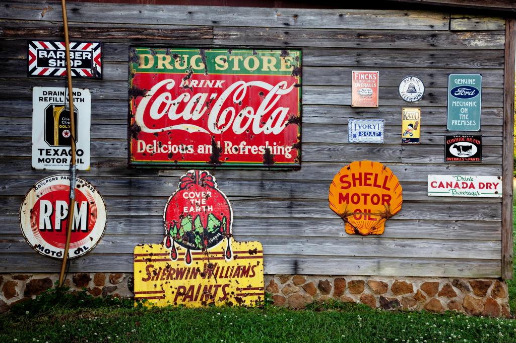 Wooden side of a building with several old advertising signs featuring some large brands.