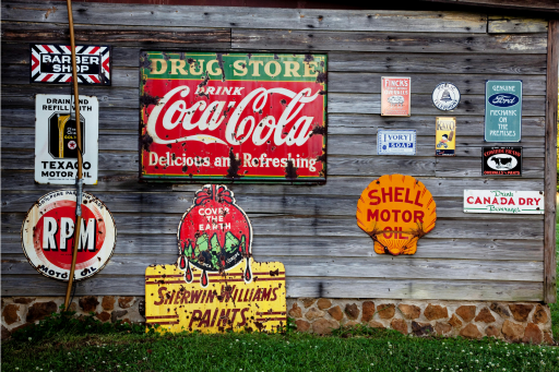 Wooden side of a building with several old advertising signs featuring some large brands.